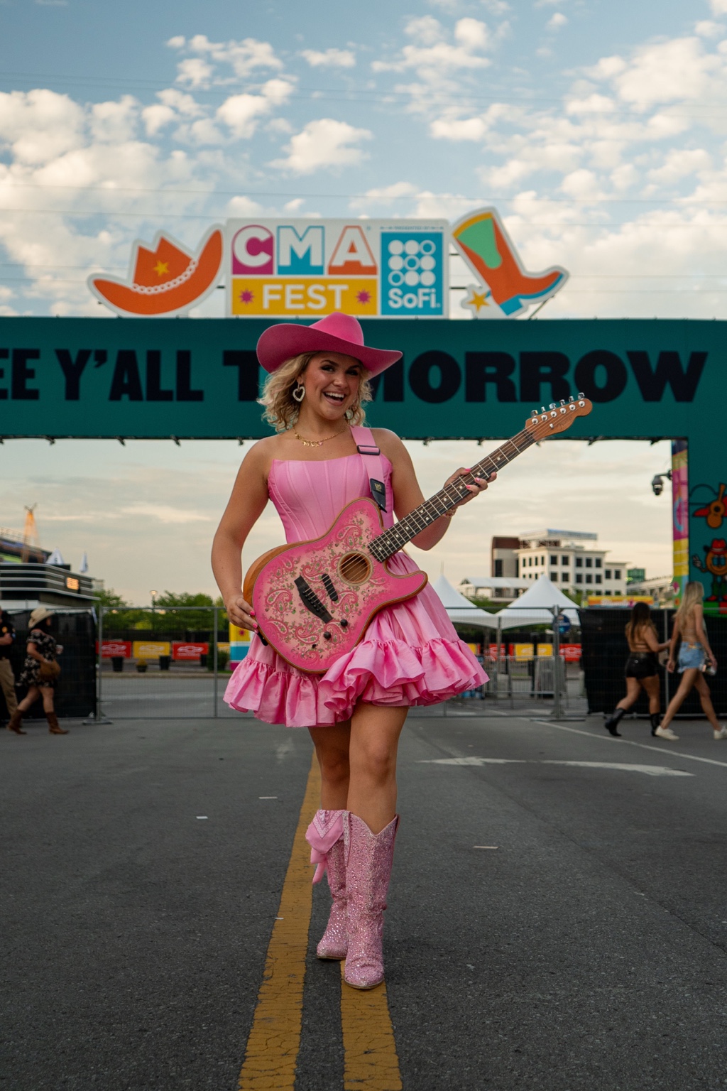 McKayla Mae Prew in a pink cowgirl hat, dress and boots, holding her pink guitar at CMA Fest